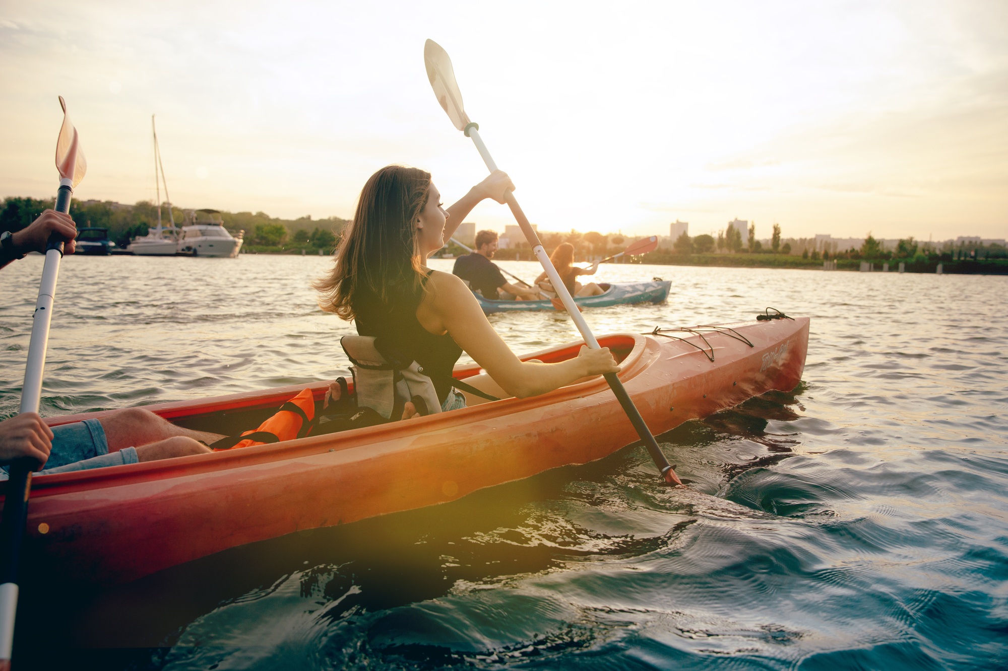 Happy friends kayaking on river with sunset on the background